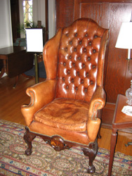 Rococo style mahogany styled wing-back chair with brown leather upholstery and tufted back with riveted edges.